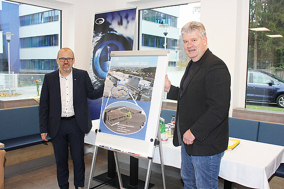 Stefan Hauptmann, General Plant Manager ZKW Lichtsysteme Wieselburg und Bürgermeister Josef Leitner stehen vor einem Clipboard und präsentieren das neue Mobilitätskonzept.
