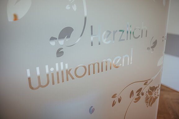 Der freundlich gestaltete Eingangsbereich, an einer Glasfront sind die Worte "Herzlich Willkommen" dargestellt 