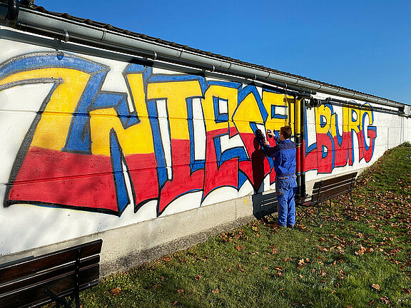 Ein Teilnehmer eines Workshops fertigt gerade ein Kunstwerk an einer Wand an.