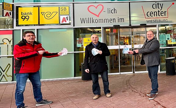 CityCenter Manager Dietmar Affengruber und der Vorsitzende des Stadtmarketings Wieselburg Josef Lechner übergeben dem Gewinner des 2. Preises Herrn Leopold Hürner seinen Gewinn. Sie stehen dabei im Freien vor dem Eingang zum CityCenter.