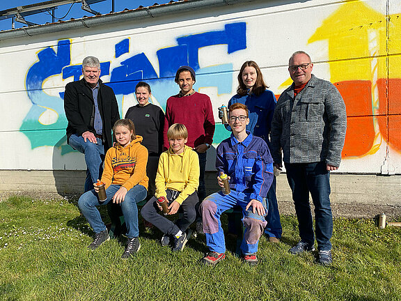 Die jugendlichen Teilnehmer am Workshop stehen gemeinsam mit dem Leiter des Projektes Florian Nährer, Bürgermeister Josef Leitner und Vizebürgermeister Peter Reiter vor einer der gestalteten Wände.